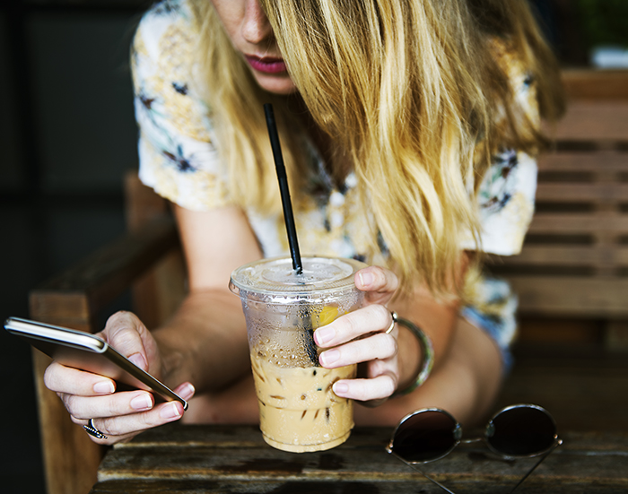 young woman using smartphone with coffee in hand
